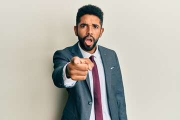 Handsome hispanic man with beard wearing business suit and tie pointing displeased and frustrated to the camera, angry and furious with you