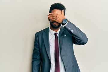 Handsome hispanic man with beard wearing business suit and tie covering eyes with hand, looking serious and sad. sightless, hiding and rejection concept