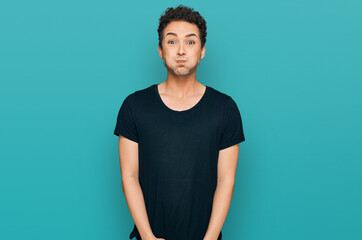 Young handsome man wearing casual black t shirt puffing cheeks with funny face. mouth inflated with...