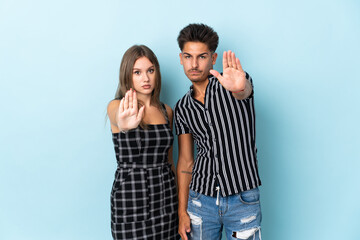 Teenager caucasian couple isolated on blue background making stop gesture denying a situation that thinks wrong