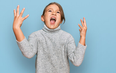 Little beautiful girl wearing casual turtleneck sweater crazy and mad shouting and yelling with aggressive expression and arms raised. frustration concept.
