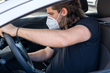 Young guy with long hair wearing a face mask by COVID-19 driving
