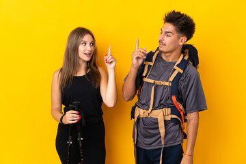 Young mountaineer couple with a big backpack isolated on yellow background intending to realizes the solution while lifting a finger up