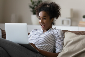 Stunned excited African American young woman use laptop shocked by unexpected sale offer or...