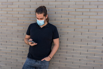 Young boy with long hair wearing a face mask by COVID-19 using his smartphone