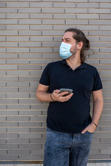 Young boy with long hair wearing a face mask by COVID-19 using his smartphone