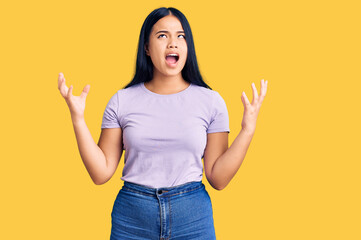 Young beautiful asian girl wearing casual clothes crazy and mad shouting and yelling with aggressive expression and arms raised. frustration concept.