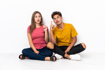 Fototapeta na wymiar Young couple sitting on the floor isolated on white background thinking an idea pointing the finger up