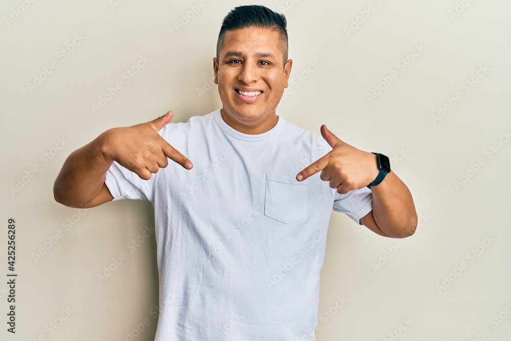 Wall mural young latin man wearing casual white t shirt looking confident with smile on face, pointing oneself 