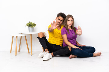 Fototapeta na wymiar Young couple sitting on the floor isolated on white background making stop gesture denying a situation that thinks wrong
