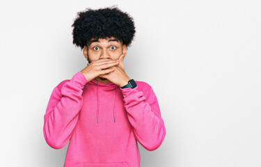 Young african american man with afro hair wearing casual pink sweatshirt shocked covering mouth with hands for mistake. secret concept.