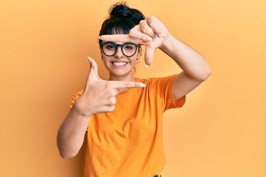 Young hispanic girl wearing casual clothes and glasses smiling making frame with hands and fingers with happy face. creativity and photography concept.