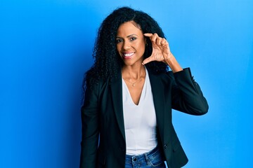 Middle age african american woman wearing business clothes smiling and confident gesturing with hand doing small size sign with fingers looking and the camera. measure concept.