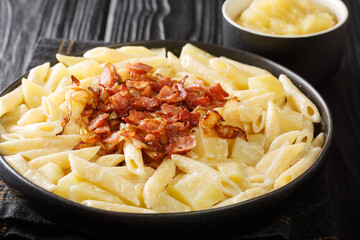 Swiss alplermagronen is pasta with potatoes and cheese topped with fried onions, bacon close-up on the table. horizontal