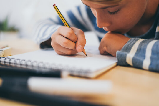 Student drawing with pencil on the notebook. Boy doing homework writing on a paper. Kid hold a pencil and draw a manga at home. Teen drawing sitting at the table. Education art talent ability concept.