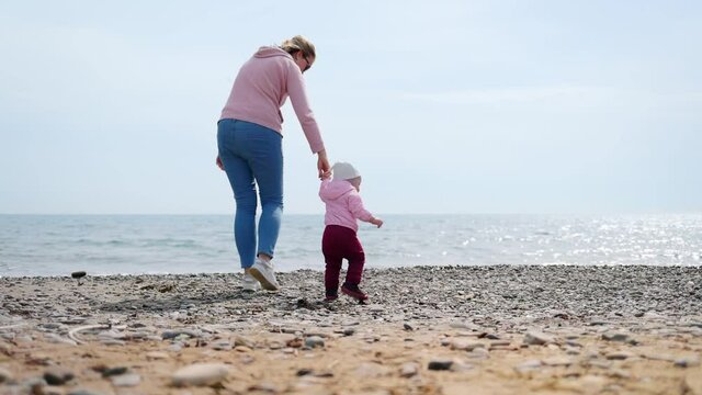 A mother leads the baby by the arm to the sea. Outdoor walks. Real time.