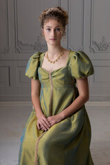 A young Regency woman wearing a green silk shot dress and tiara and sitting in a paneled room © Kathy