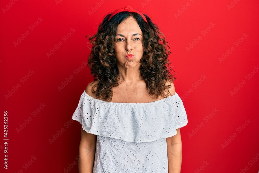 Wall mural Middle age hispanic woman wearing casual clothes puffing cheeks with funny face. mouth inflated with air, crazy expression.