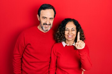 Naklejka premium Middle age couple of hispanic woman and man hugging and standing together showing and pointing up with finger number one while smiling confident and happy.