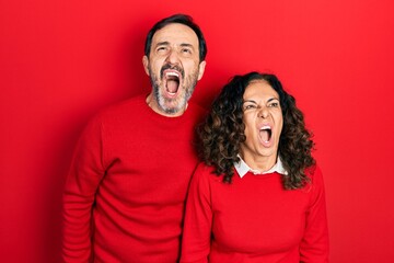 Middle age couple of hispanic woman and man hugging and standing together angry and mad screaming...