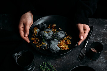 Black dumplings with potatoes and onions in a plate. Dark photo