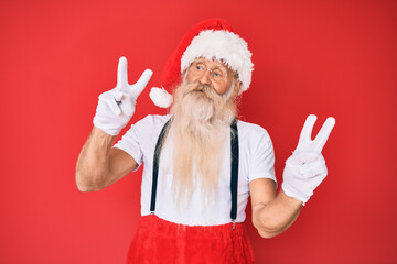 Fototapeta na wymiar Old senior man with grey hair and long beard wearing white t-shirt and santa claus costume smiling looking to the camera showing fingers doing victory sign. number two.