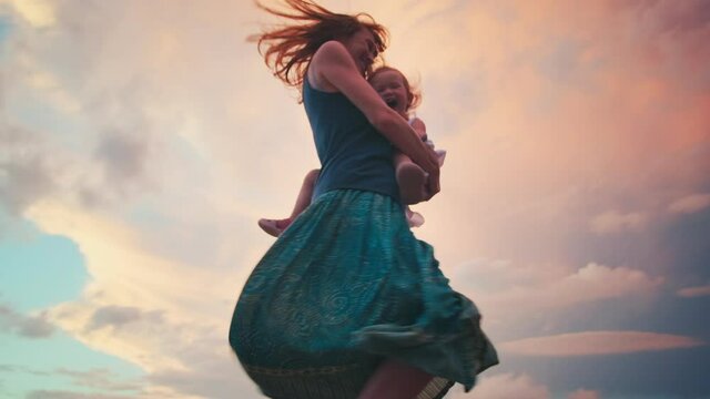 Family dances on pier. Woman and toddler girl dance and spin on the wooden pier during sunset