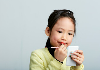 Asian little girl doing makeup on herself in fun