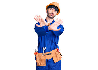Young hispanic man wearing worker uniform rejection expression crossing arms and palms doing negative sign, angry face