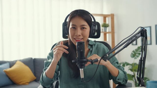 Happy asia girl record a podcast with headphones and microphone look at camera  talk and take a rest in her room. Female podcaster make audio podcast from her home studio, Stay at house concept.
