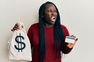 Young black woman with braids holding dollars bag and credit card angry and mad screaming...