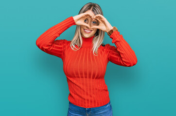 Beautiful blonde woman wearing casual clothes doing heart shape with hand and fingers smiling looking through sign