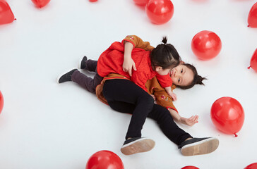 Cute Asian little girls playing with festive red balloons. Wearing traditional Chinese New Year costumes