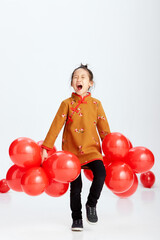 Fototapeta na wymiar Cute Asian little girl playing with festive red balloons. Wearing traditional Chinese New Year costumes