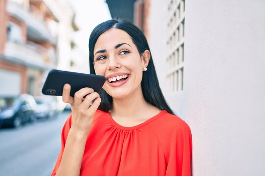 Young latin girl smiling happy sending voice message using smartphone at the city.