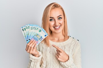 Beautiful caucasian blonde woman holding 20 euro banknotes smiling happy pointing with hand and finger