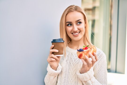 Young blonde girl smiling happy having breakfast standing at the city.