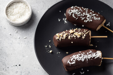 Bananas in dark chocolate with nuts and coconut on dark plate. Frozen healthy dessert. close-up