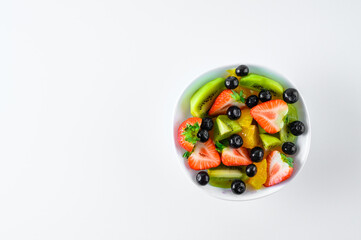 Sliced fresh ripe fruit (strawberries, kiwis, citrus fruits, blueberries) on a white plate. White background.