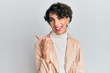 Young man wearing woman make up and woman clothes pointing thumb up to the side smiling happy with...