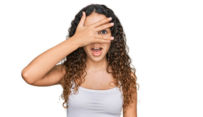 Teenager hispanic girl wearing casual clothes peeking in shock covering face and eyes with hand, looking through fingers with embarrassed expression.