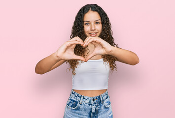 Teenager hispanic girl wearing casual clothes smiling in love doing heart symbol shape with hands. romantic concept.