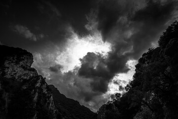 DRAMATIC CLOUDS ABOVE SLOPES. Black and white view on sunlight mountains in clouds.
