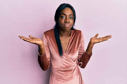 Young african american woman wearing sexy party dress clueless and confused with open arms, no idea and doubtful face.