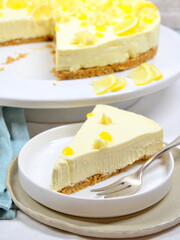 Lemon Curd Cheesecake auf Tortenplatte, ein Stück abgeschnitten und auf Teller