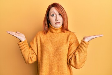 Beautiful redhead woman presenting with open palm skeptic and nervous, frowning upset because of...