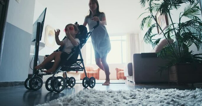 Family have fun in room. Mother gives her toddler girl a ride on the baby stroller along the rooms in apartment