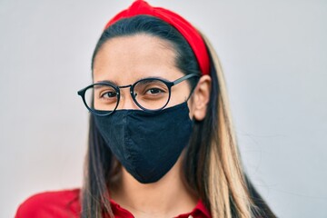 Young hispanic woman wearing coronavirus protection mask standing at the city.