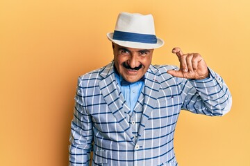 Mature middle east man with mustache wearing vintage and elegant fashion style smiling and confident gesturing with hand doing small size sign with fingers looking and the camera. measure concept.