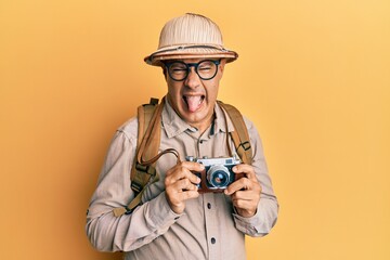 Middle age bald man wearing explorer hat and vintage camera sticking tongue out happy with funny...